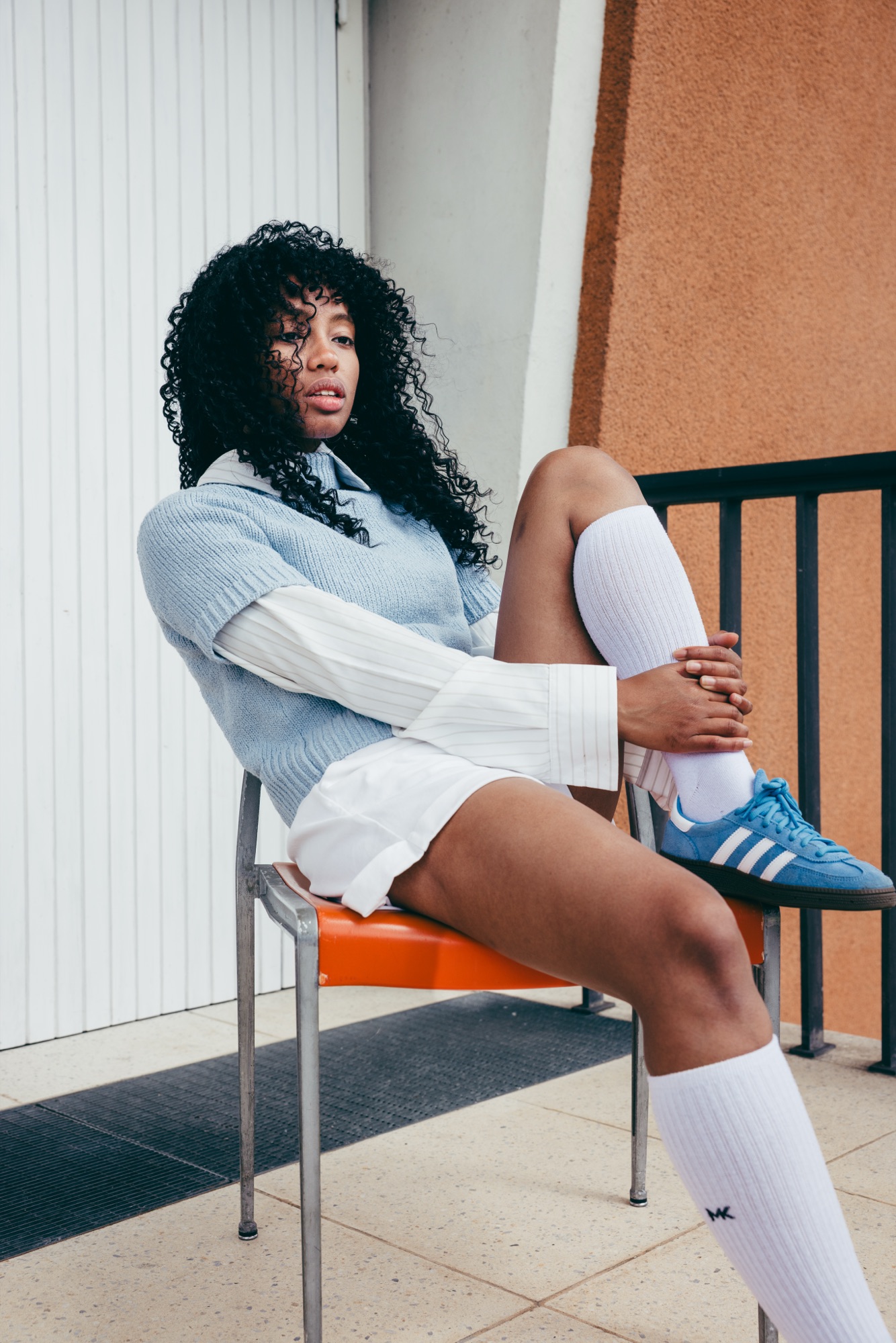 Adidas Originals Court Study – Profil-Aufnahme auf vintage-orangem Stuhl mit weißem Layering und blauem Sneaker von Kürsat Gürbüz