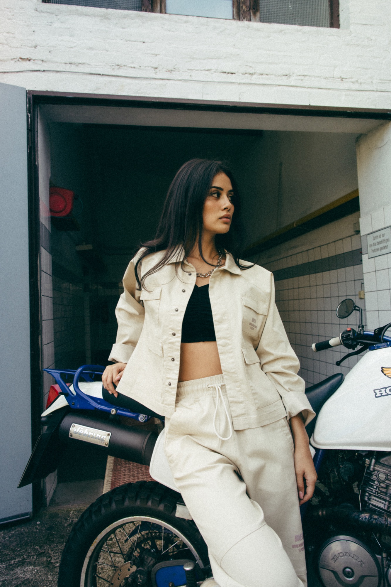 DEFSHOP – Model in beiger Workwear angelehnt an Motorrad auf Outdoor-Location