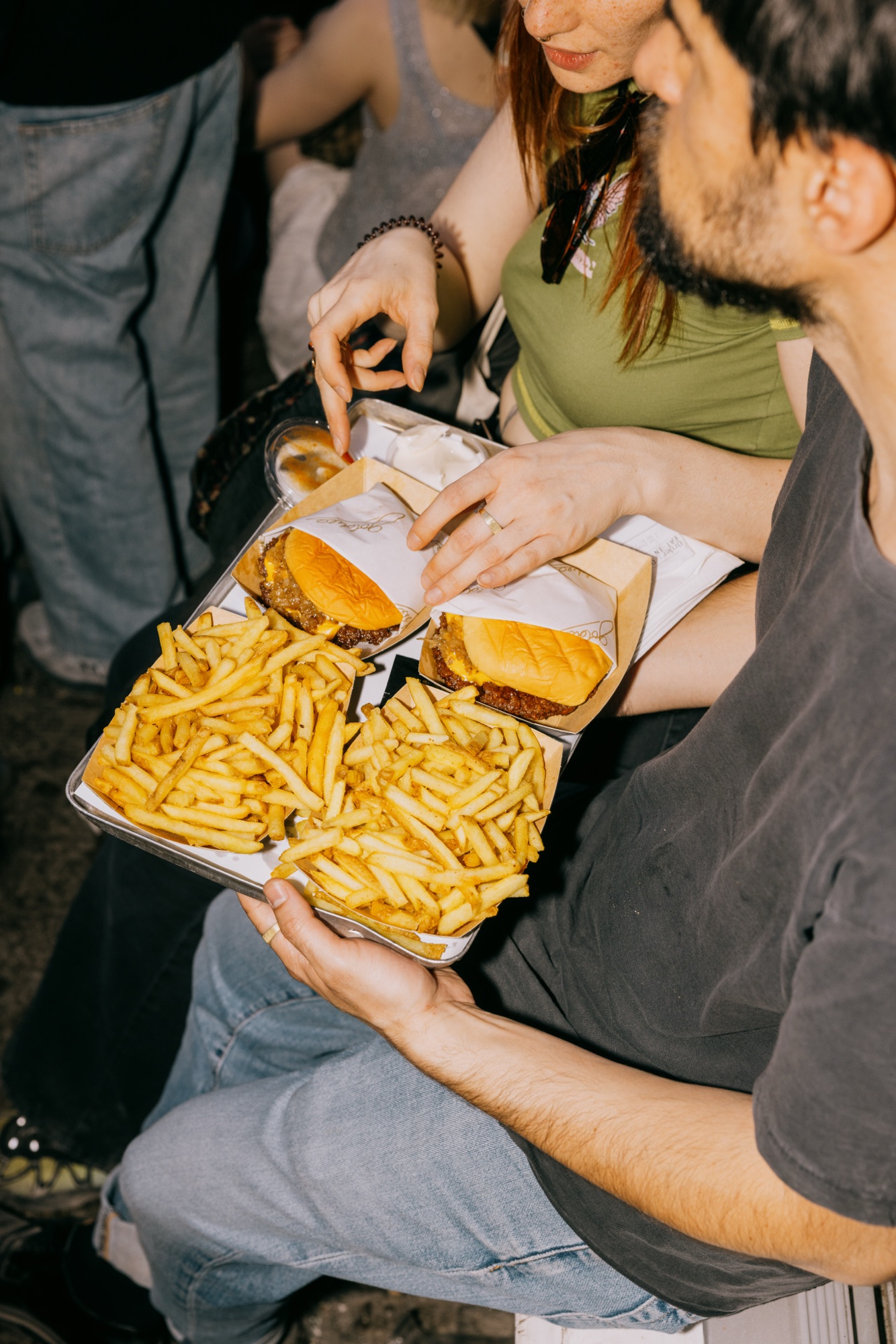 Goldies 1. Mai Fest – Gast hält Tablett mit Smashburgern und Pommes im Sitzen auf der Straße von Kürsat Gürbüz