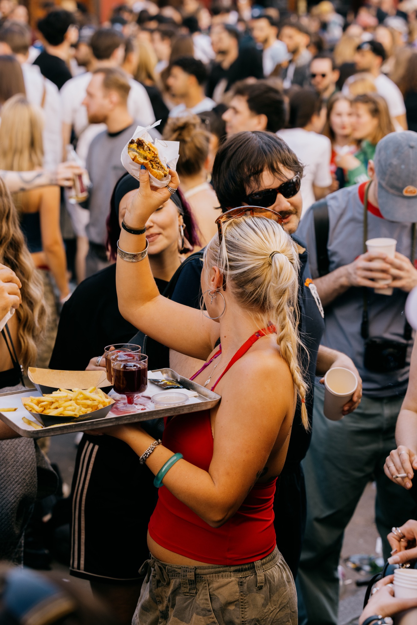 Goldies 1. Mai Fest – Gästin hebt stolz einen Smashburger in die Luft und trägt Tablett durch die Menge von Kürsat Gürbüz