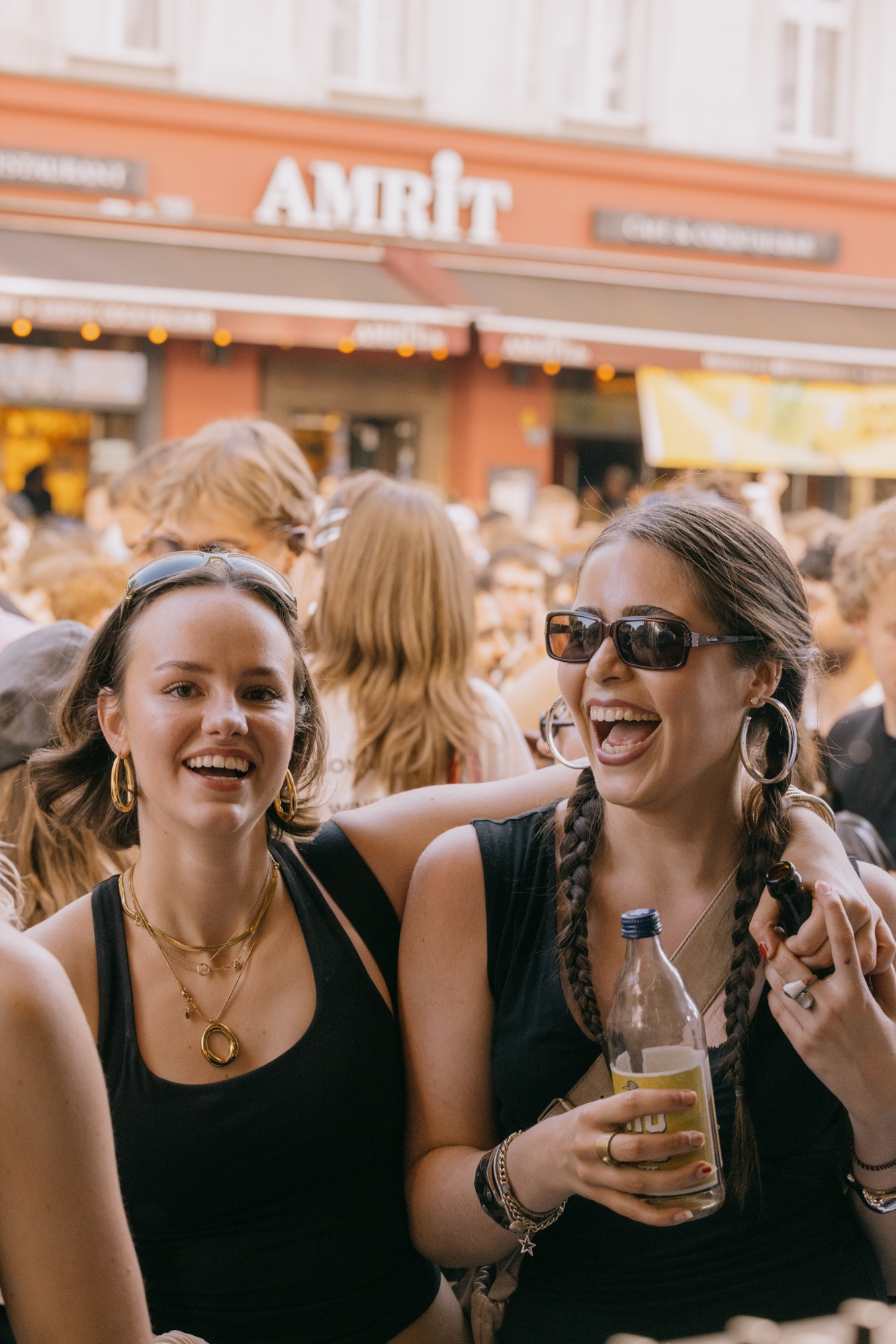 Goldies 1. Mai Fest – Zwei Freundinnen lachen ausgelassen in der sonnigen Straßenfest-Menge von Kürsat Gürbüz