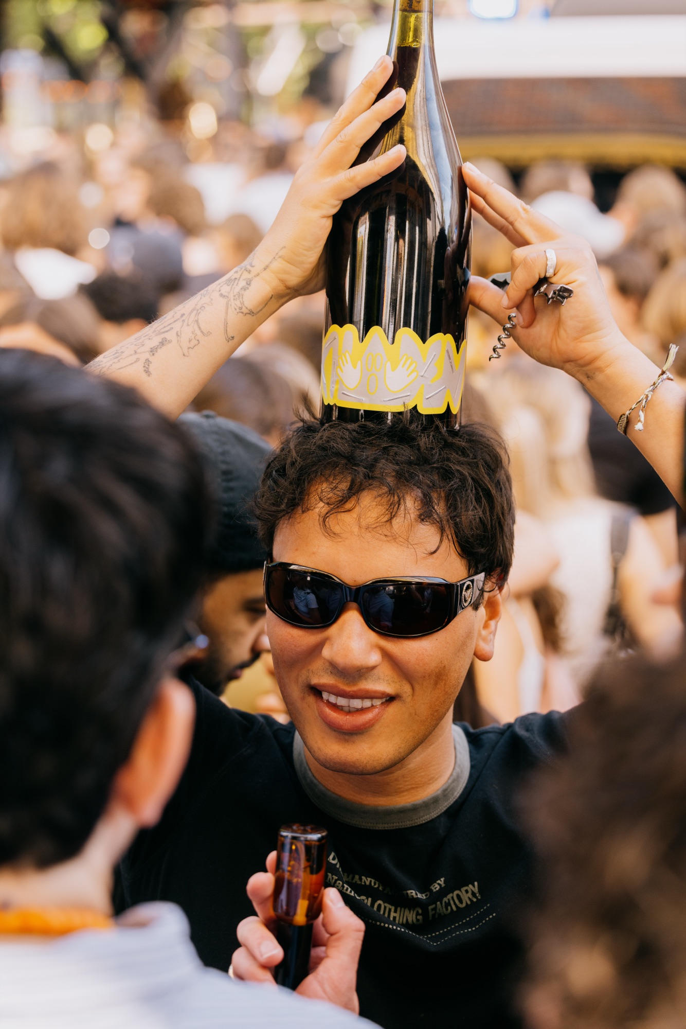 Goldies 1. Mai Fest – Gast balanciert lachend eine Magnumflasche Naturwein auf dem Kopf von Kürsat Gürbüz
