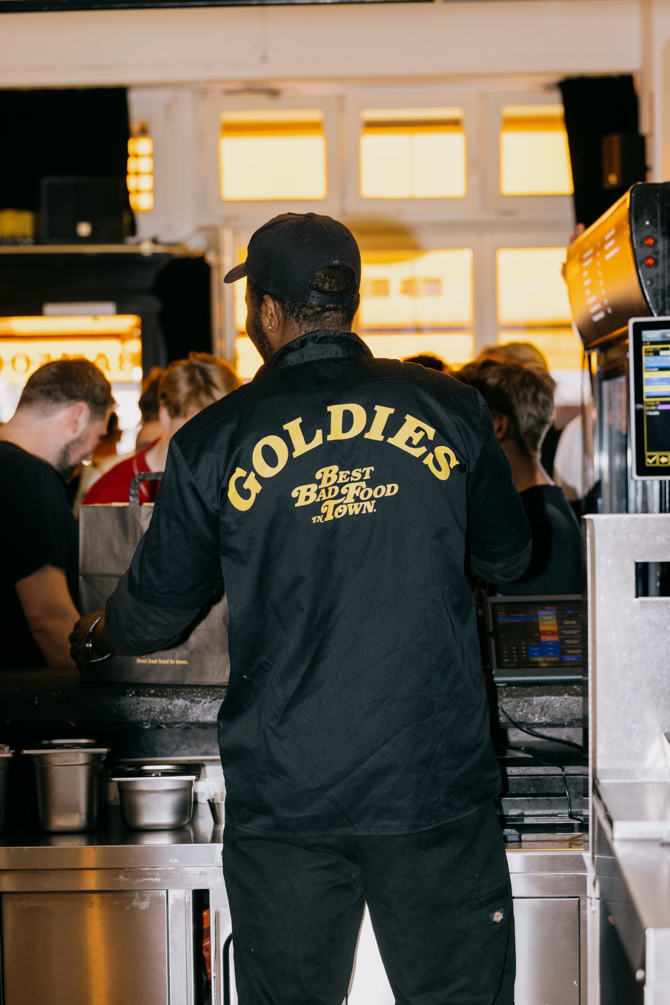 Goldies 1. Mai Fest – Goldies Mitarbeiter von hinten im gebrandeten Team-Shirt am Tresen von Kürsat Gürbüz