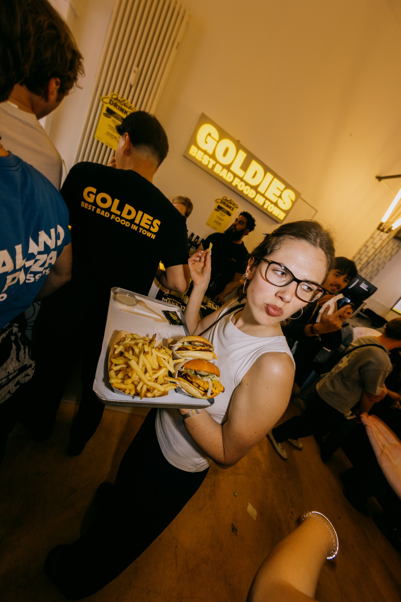 Goldies 1. Mai Fest – Kundin balanciert Tablett mit Smashburgern und Pommes unter der Goldies Neonschrift von Kürsat Gürbüz