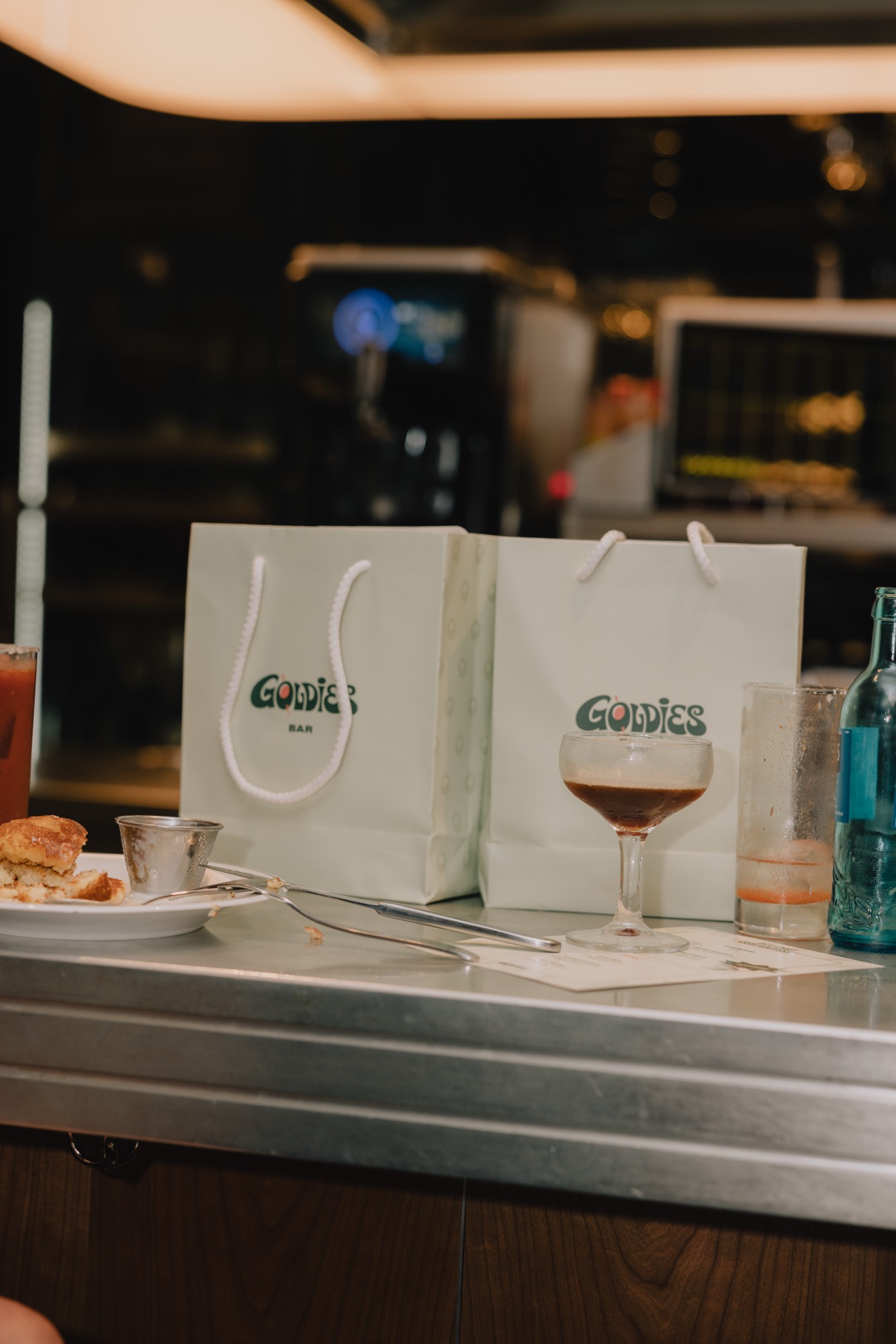 Goldies Bar Breakfast Launch – Gebrandete Papiertüten und Cocktailglas auf dem Tresen von Kürsat Gürbüz