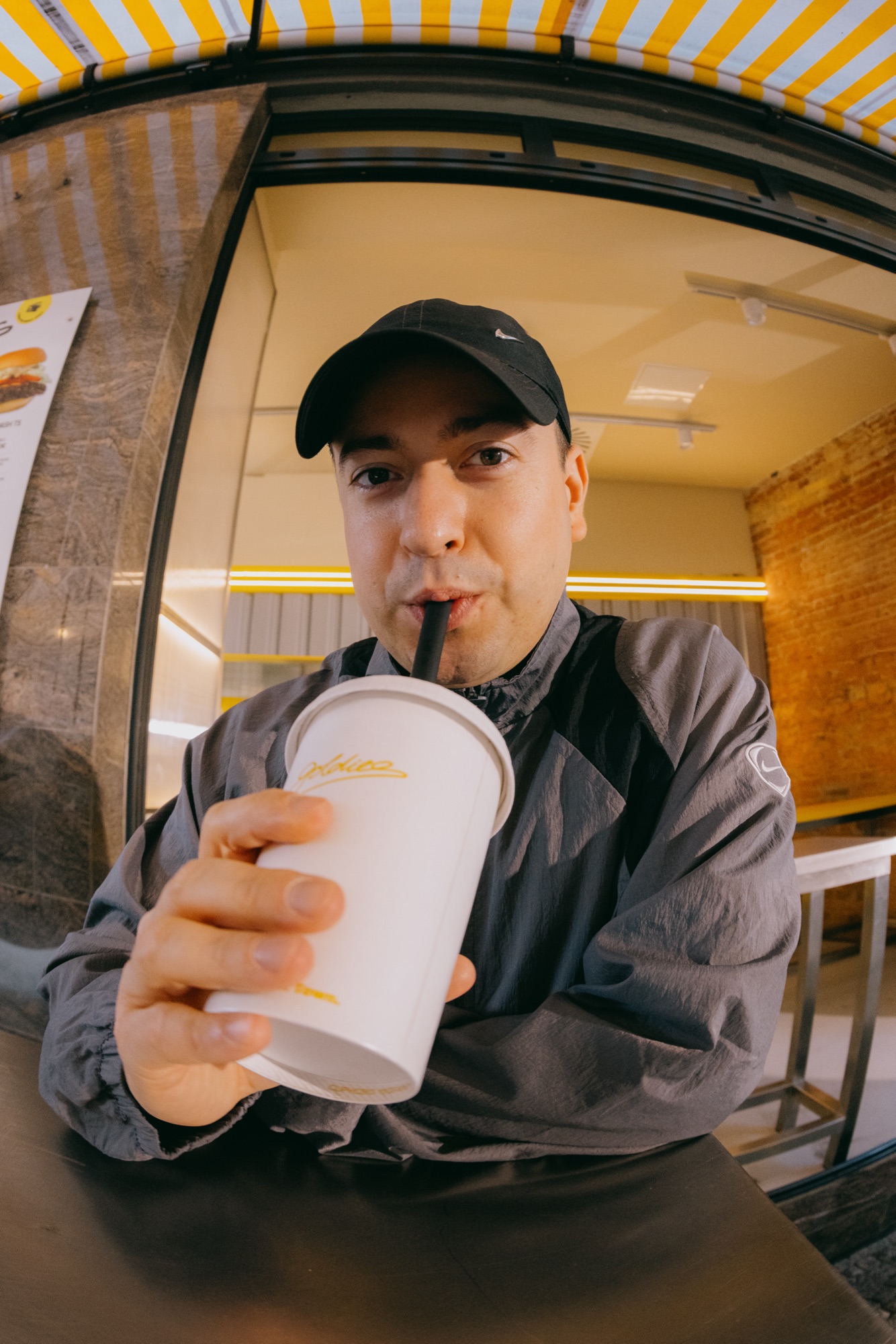 Goldies Kampagne – Fisheye-Porträt eines Mannes mit Cap beim Trinken eines Milkshakes vor dem Store von Kürsat Gürbüz
