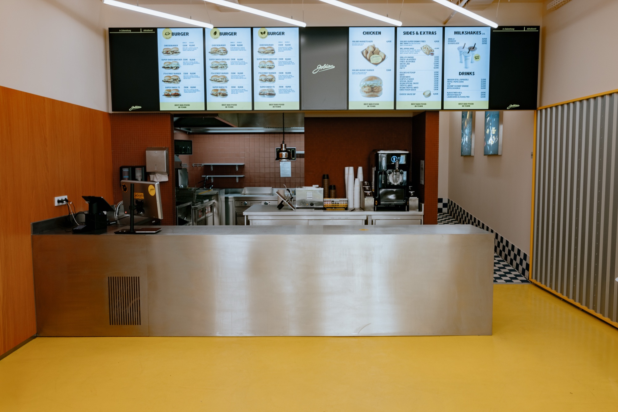 Goldies Schöneberg – Offene Edelstahl-Bestelltheke mit digitalen Menüboards und Blick in den Küchenbereich von Kürsat Gürbüz