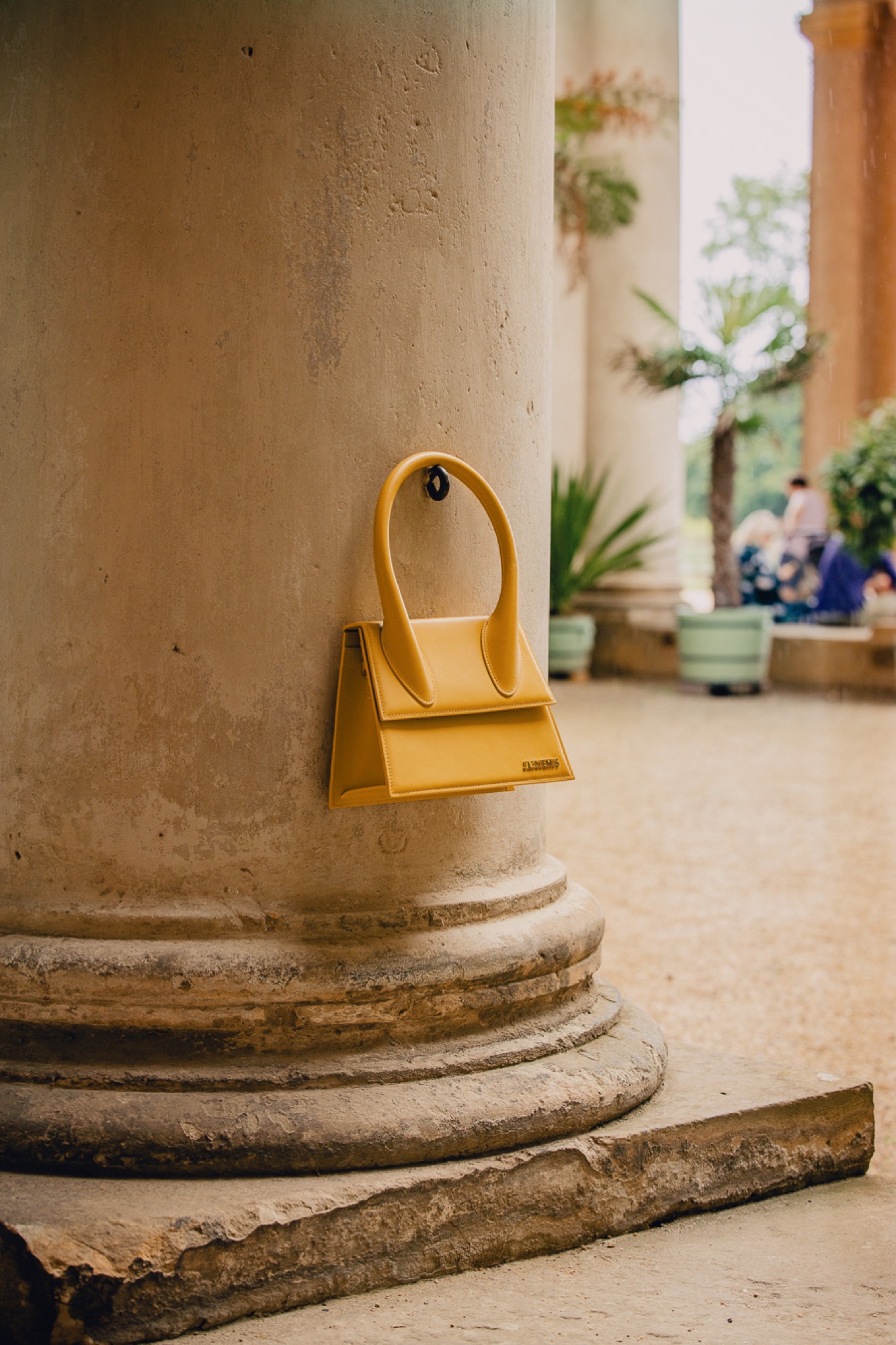 Jacquemus Summer Study – Gelbe Le Chiquito Tasche an Steinsäule von Kürsat Gürbüz