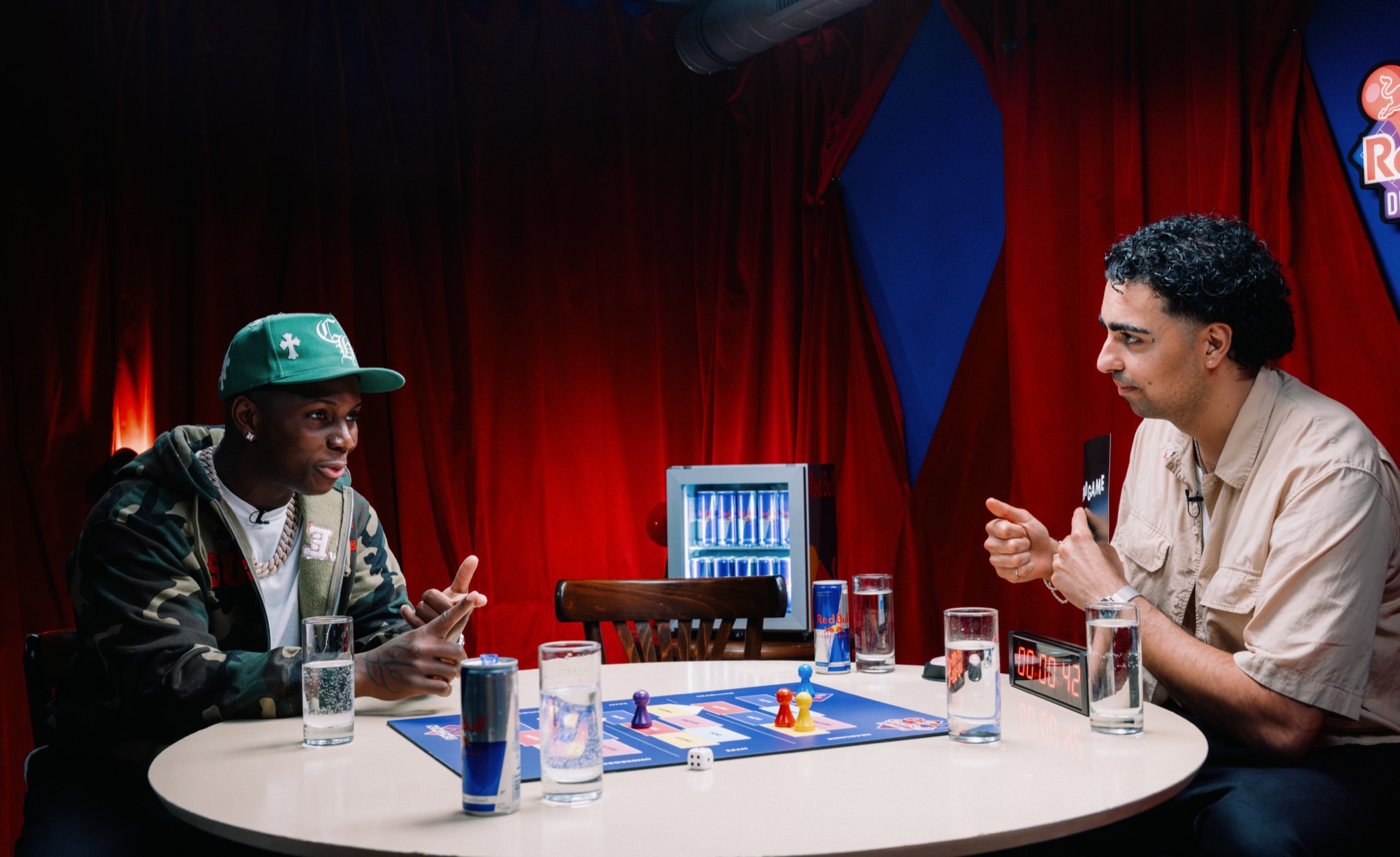 Red Bull Durchgespielt – Dialog am Tisch vor dem Red-Bull-Kühlschrank von Kürsat Gürbüz