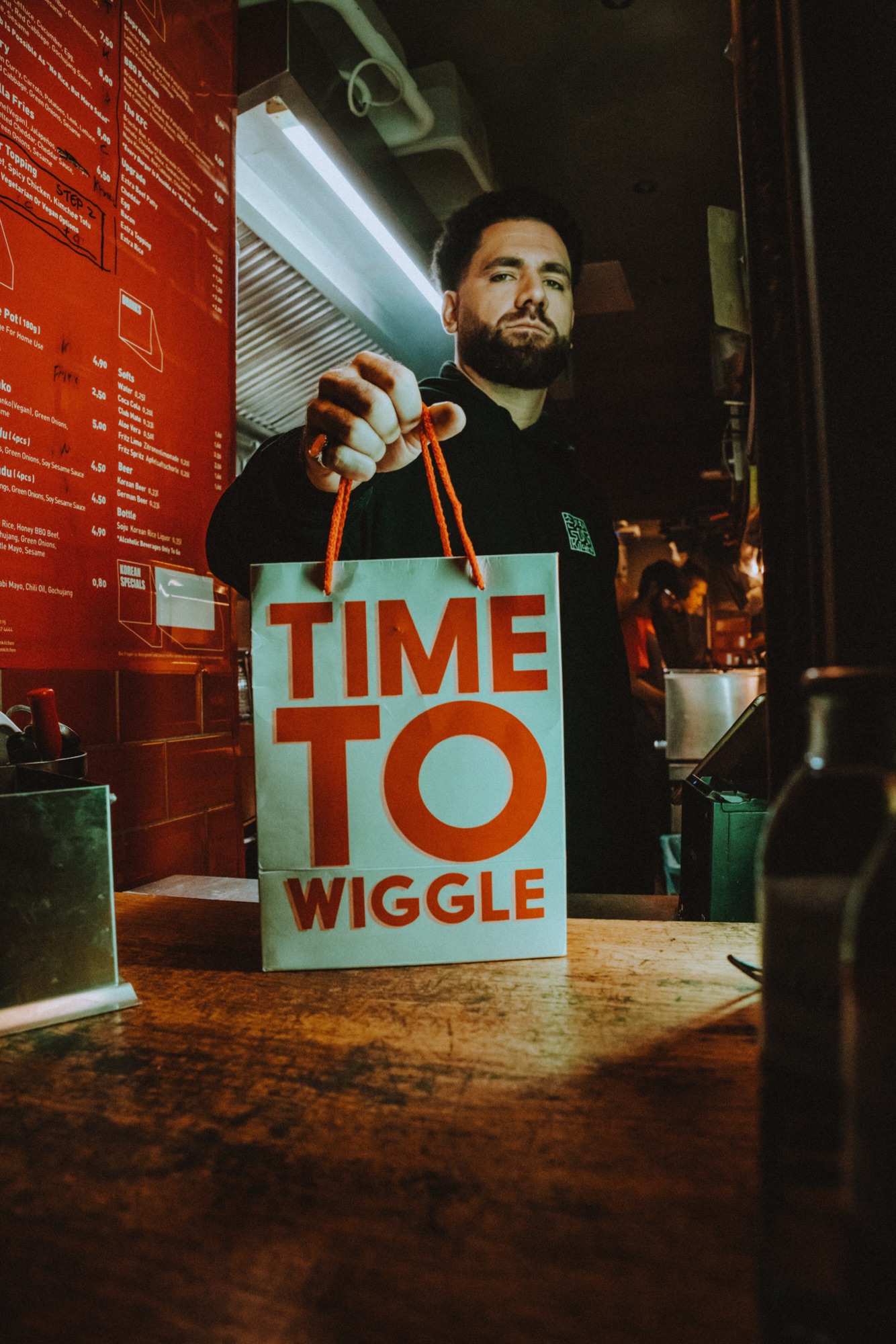 Wiggle Steps – Mitarbeiter reicht Time to Wiggle Papiertüte über Food-Counter von Kürsat Gürbüz